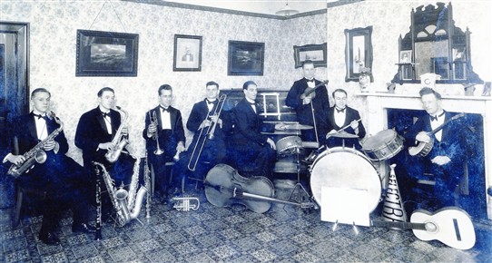 Photo:Len Coyne's "Selectra" Band c.1930 pictured in what became the Coyne family's living room on the first floor of the Moot Hall.  Photographed in a room above the shop, the picture shows Len Coyne (second from left) and Frank Coyne on drums.  Arthur Coyne is 4th from left.  Note the loud-hailer (next to the bass drum) which was used by the vocalist in these days before microphones.